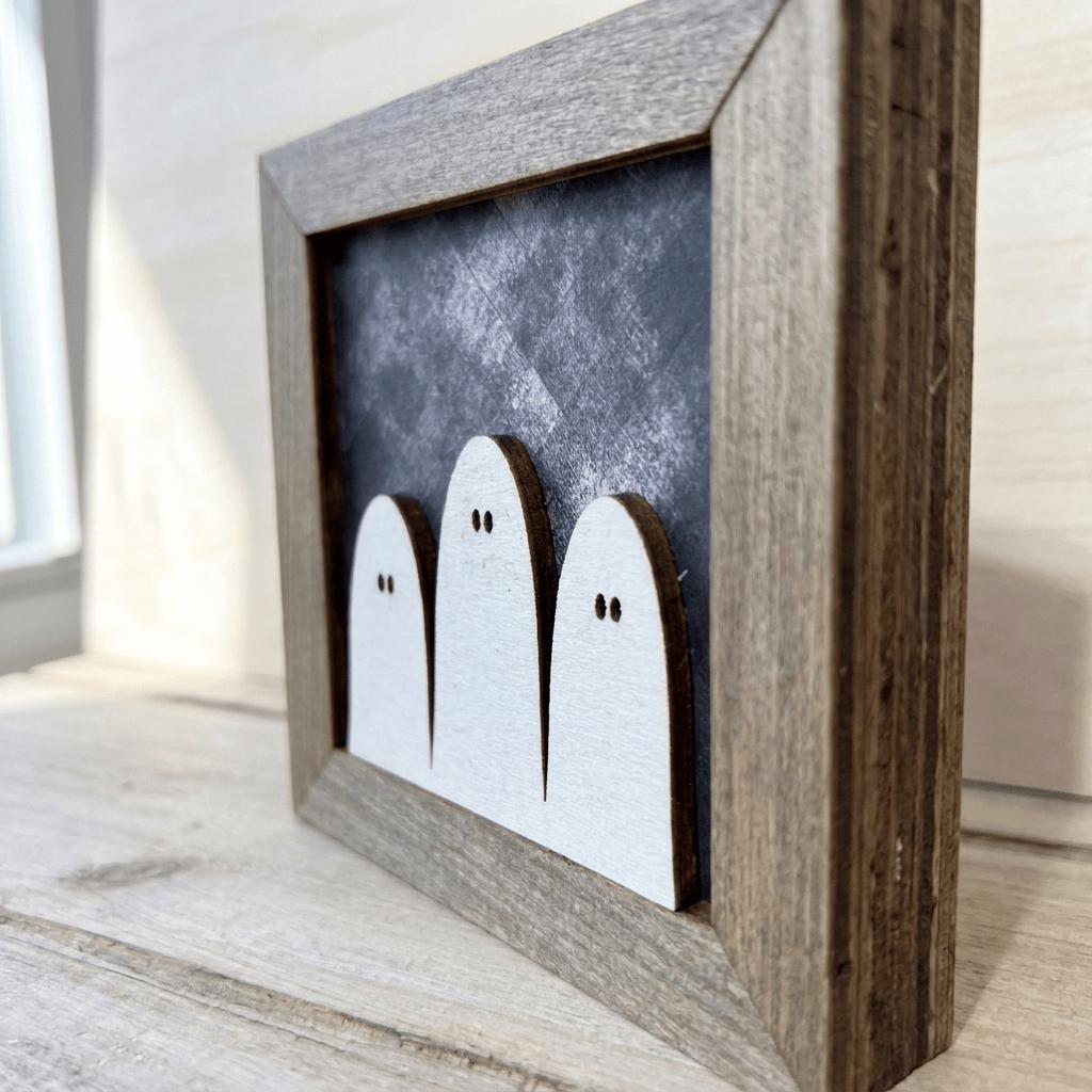 A wooden frame containing three white ghost-like figures against a dark background.