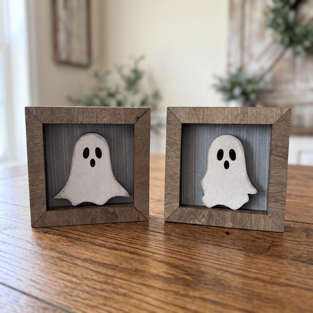 Two small wooden frames containing ghost-like silhouettes are placed on a wooden surface.