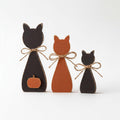 Three wooden cat figurines are arranged in a row, each with a pumpkin attached to their backs.