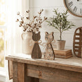 a rustic wooden table with various decorative items on it, including wooden cat figurines, a vase of cotton bolls, and a potted plant. There is also a clock hanging on the wall above the table.