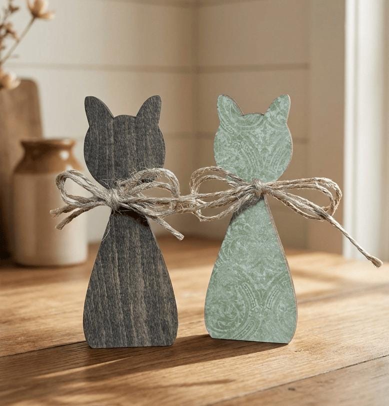 Two wooden cat figurines, one black and one green, are tied together with a string on a wooden surface.
