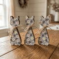 Three wooden cat figurines with floral patterns are arranged on a wooden surface, tied with twine.