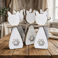 a group of white wooden cat-shaped ornaments, each adorned with a snowflake design, arranged on a wooden surface.