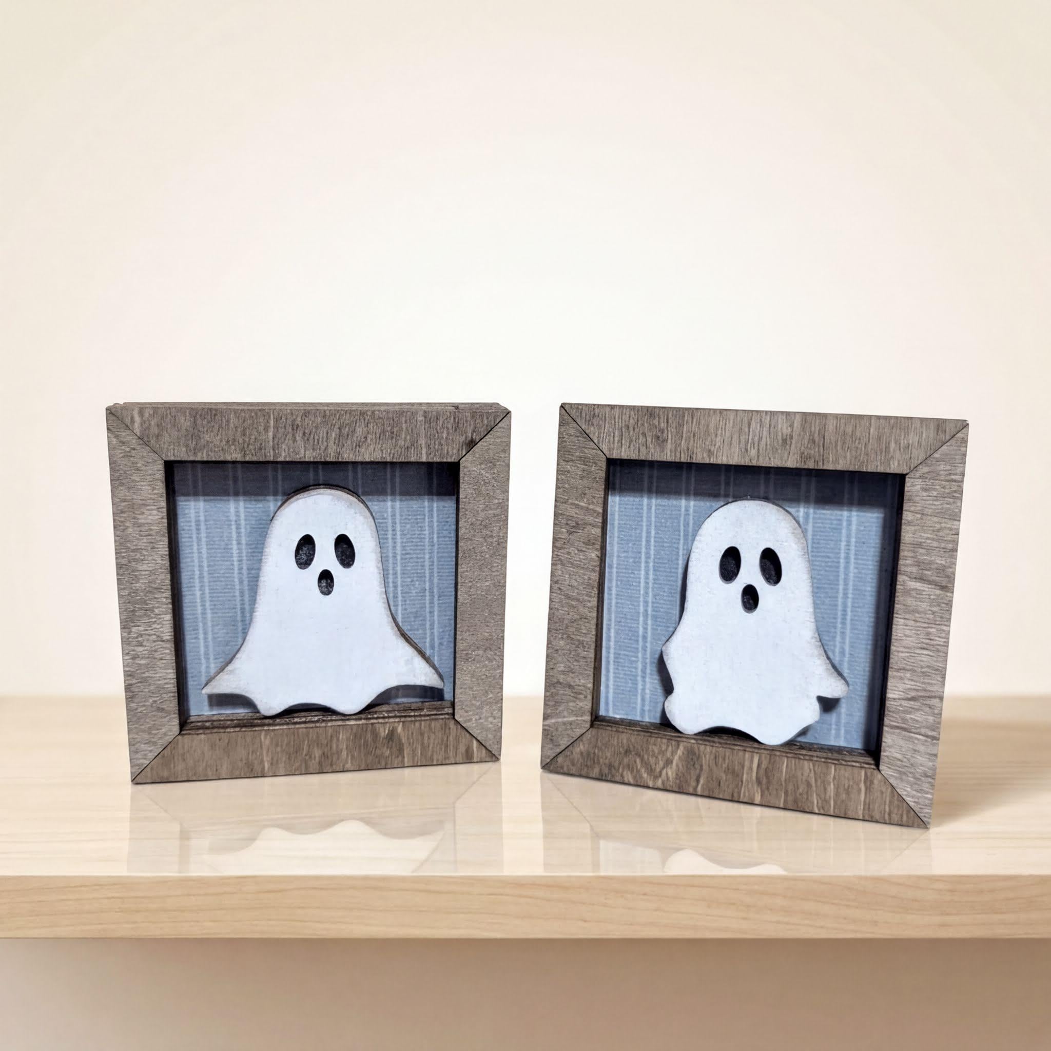 Two wooden frames containing ghost-like figures are placed on a wooden surface.