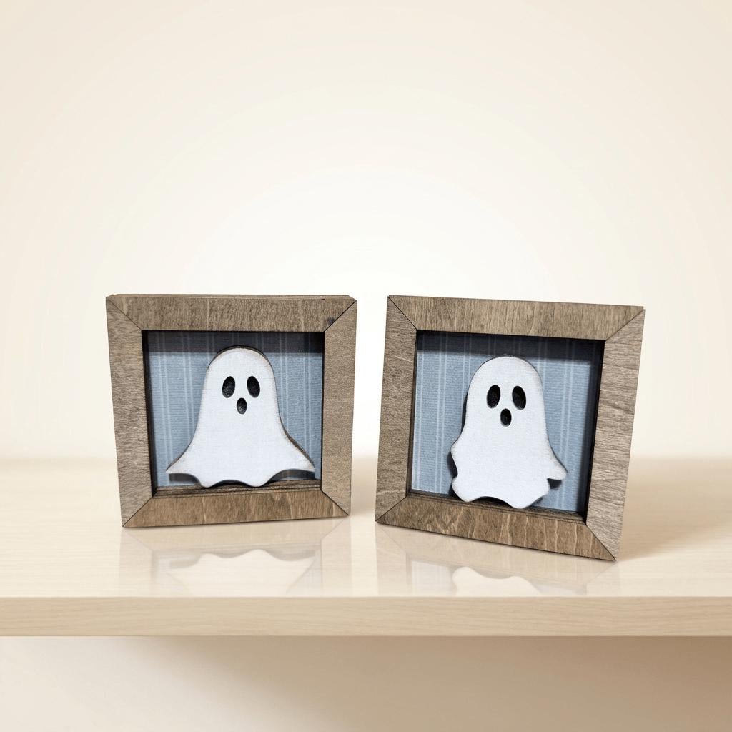 Two wooden frames containing white ghost-like figures are placed on a light-colored surface.