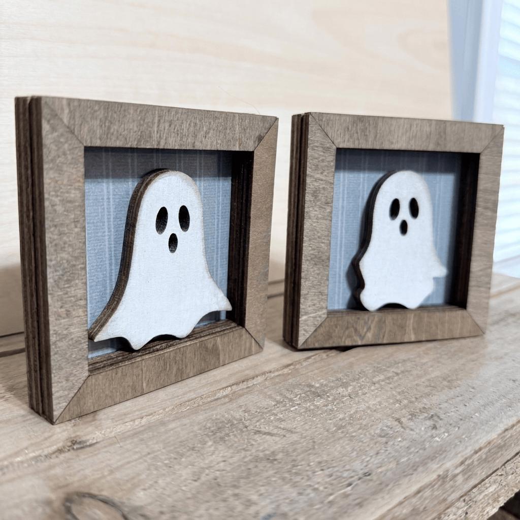 two wooden frames with ghost-like silhouettes inside them, placed on a wooden surface.