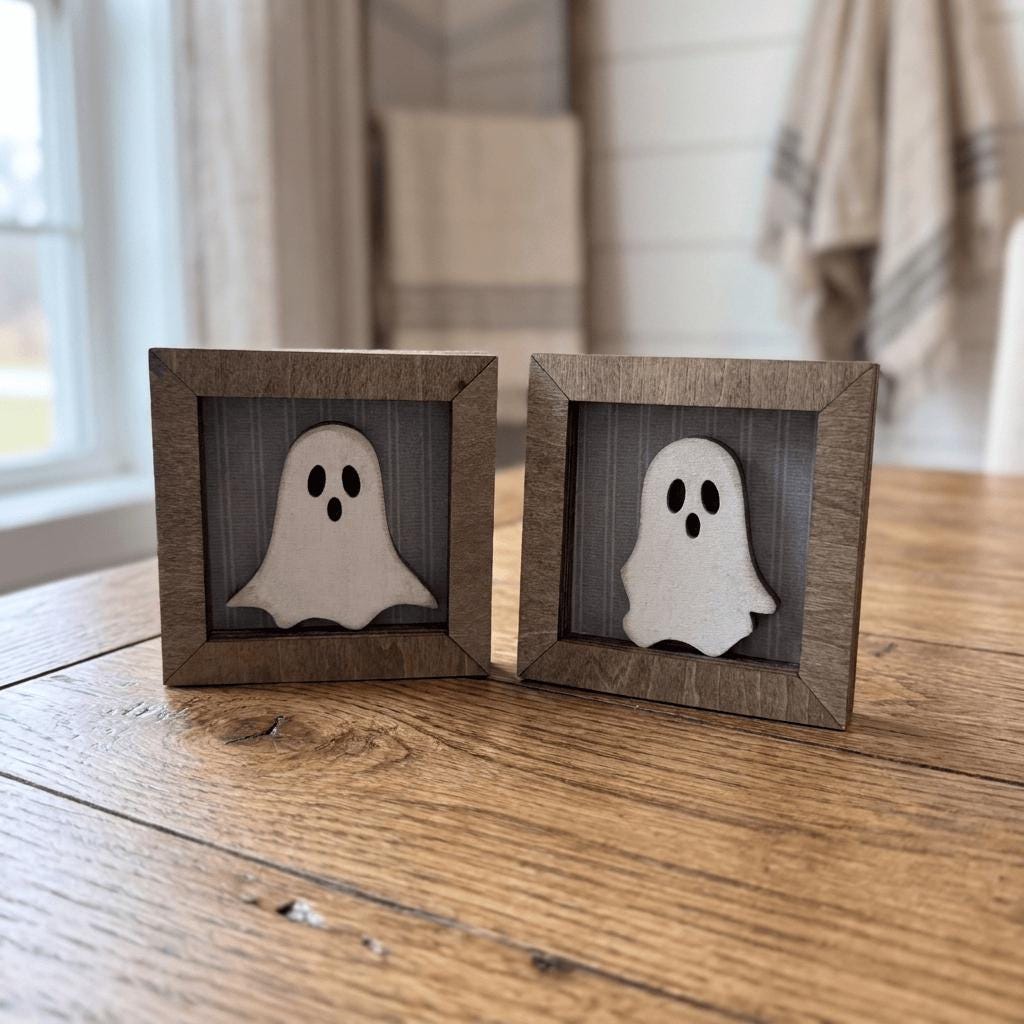 Two small wooden frames with ghost-like silhouettes are placed on a wooden surface.