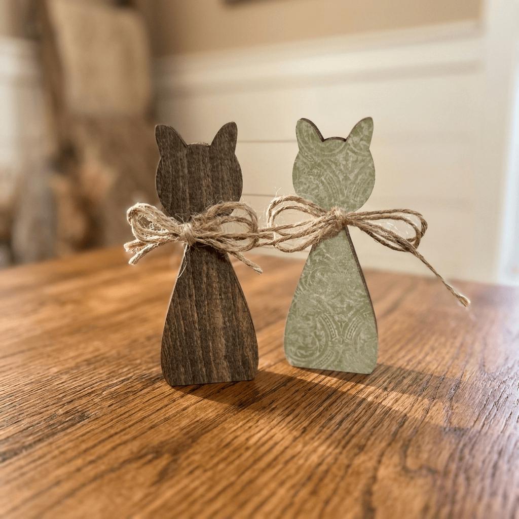 Two wooden cat figurines tied together with twine on a wooden surface.