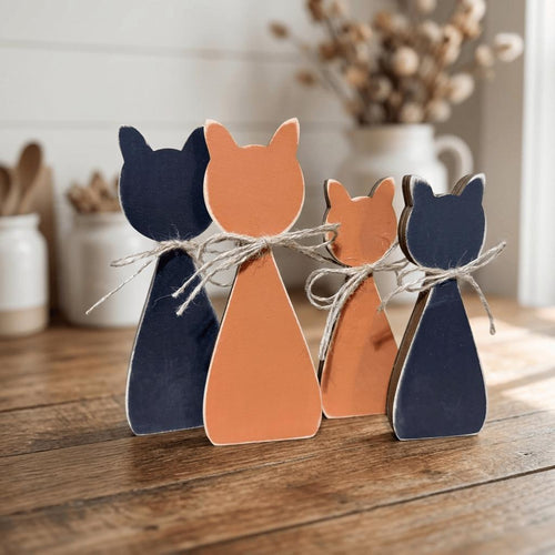Three wooden cat figurines are arranged on a wooden surface, with one cat in blue, one in orange, and one in black.